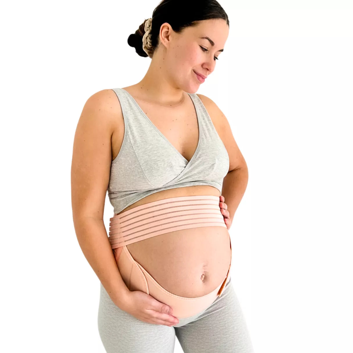 A pregnant woman wearing a belly support band in a left side view, positioned under the baby bump on a white background.