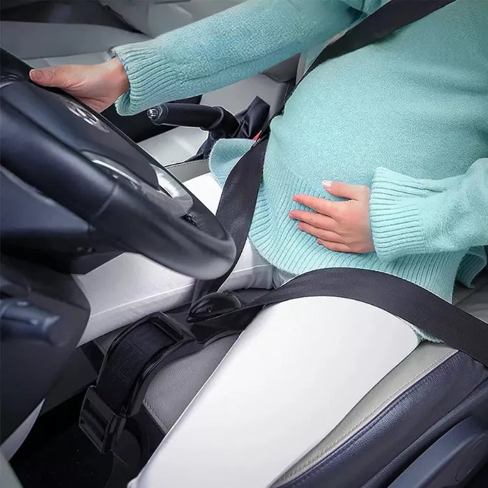 Pregnant woman driving a car using a pregnancy seat belt positioner that keeps seat belt pressure off the belly.